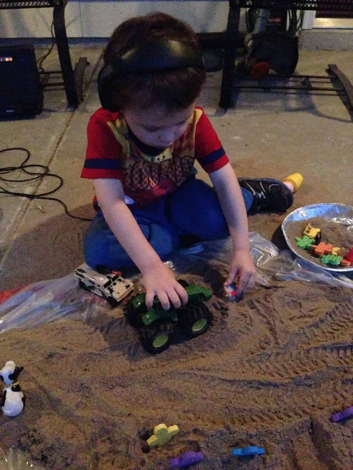 preschooler wearing headphones playing with sand toys in sand