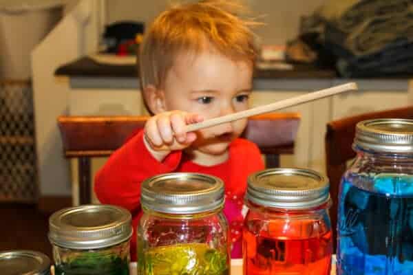 girl tapping different sizes of glass jars filled with colored water