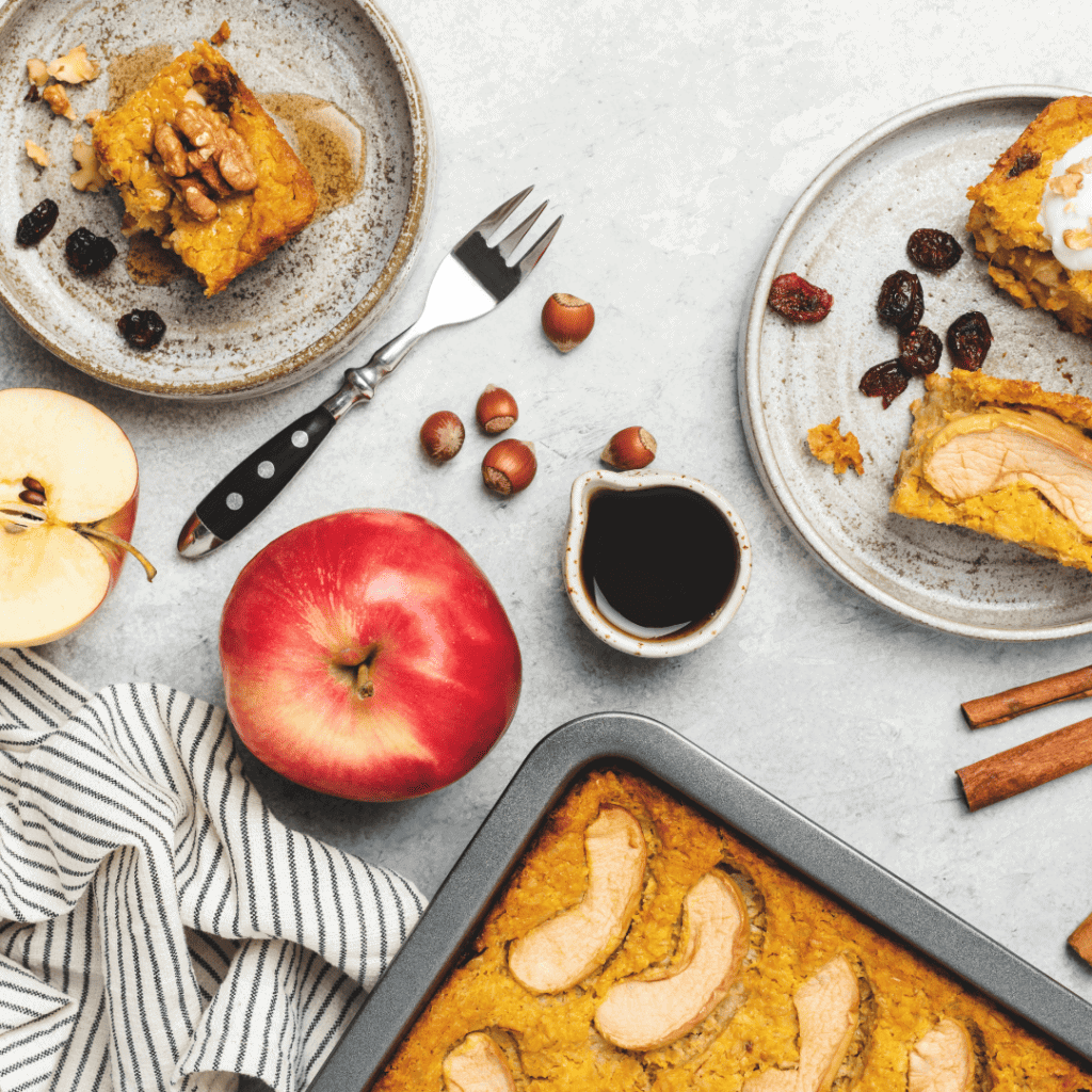 apple spice cake in  a baking dish and slices on plates with an apple and syrup sitting on the counter