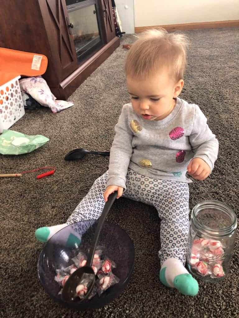 Toddler using eye movement skills to scoop peppermint candies out of a bowl using a ladle. 