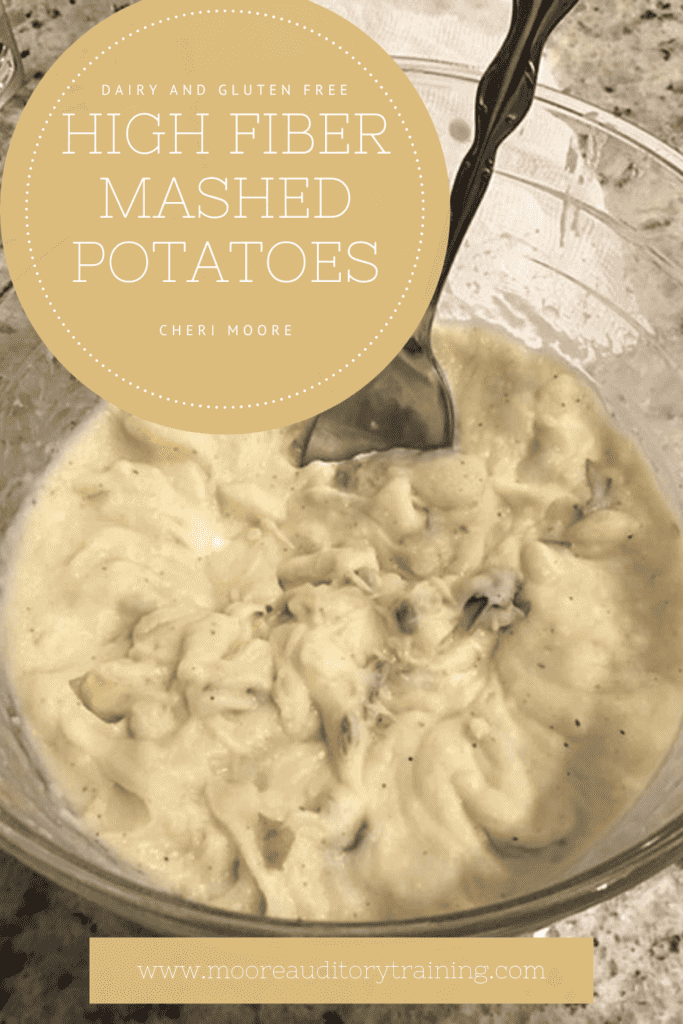 creamy high fiber dairy free mashed potatoes in a glass bowl with a spoon sticking out. The glass bowl is sitting on a grey speckled countertop. In the top left hand corner is a tan circle with white text. In the center at the bottom is another tan box with white text. 