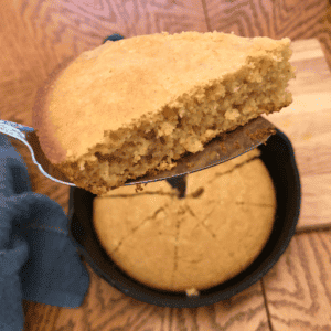 slice of gluten free cornbread held up above the skillet of hot cornbread