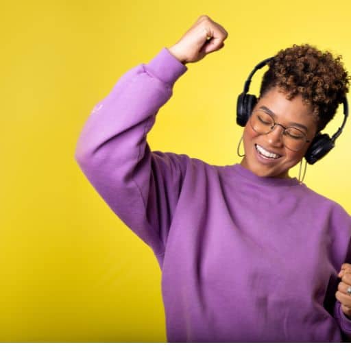 Young adult African woman wearing black headphones smiling and swaying to the music.