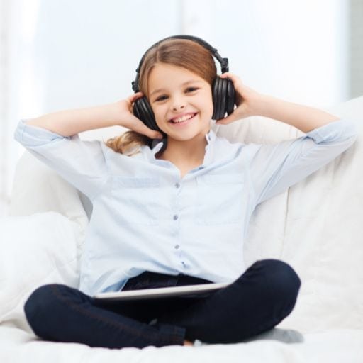 A young teen girl wearing a blue blouse sitting on her couch with a happy look on her face listening to therapeutic music called Auditory Integration Training